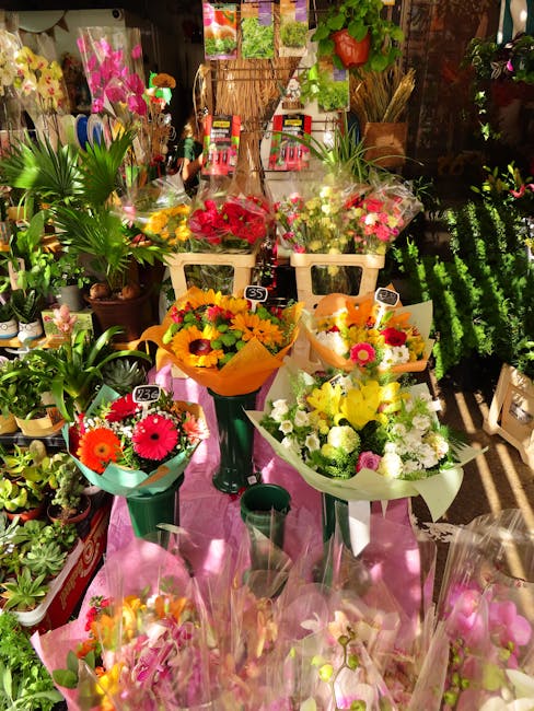 A vibrant display of fresh flower bouquets on a pink table at a florist shop, featuring a variety of colorful arrangements including red, yellow, pink, and white flowers such as gerbera daisies, roses