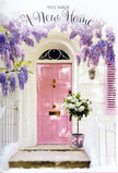 This image portrays a lovingly styled front entrance in Cheam, designed to express warmth and welcome through flowers and soft colour. At the heart of the composition is a pale pink door, its tone somewhere between blush and rose, finished in a gentle matte that absorbs the light and offers a calm, modern charm you might expect to see just off Ewell Road. The surrounding walls are painted in a crisp, whitewashed shade, their subtle imperfections catching the light and giving the scene texture and character. Flowing from above, a generous cascade of wisteria tumbles down in lavender and lilac strands, the blossoms hanging in loose, pendulous clusters that frame the doorway with natural grace. The foliage is a gentle, dusty green, weaving among the blooms and softening the arch they create. Anchoring the composition at ground level, a rounded grey metal bucket sits neatly on the doorstep, repurposed as a rustic vase for an abundant bouquet of white roses. Each rose appears lush and velvety, with layers of creamy petals unfolding in concentric swirls that suggest both delicacy and fullness. Small sprigs of fresh greenery peep out between the blooms, lending depth and a faint suggestion of woodland fragrance. Around the base of the bucket, a pink satin ribbon is tied in an easy bow, its loose ends curling slightly against the step, repeating the pink tones of the door and tying the whole arrangement together visually. The light is soft and slightly golden, falling across the petals and paintwork in a way that feels peaceful and hopeful. The scene seems perfectly suited to a housewarming in Cheam, capturing the quiet excitement, tenderness, and sense of promise that accompany opening the door to a new chapter of home life.